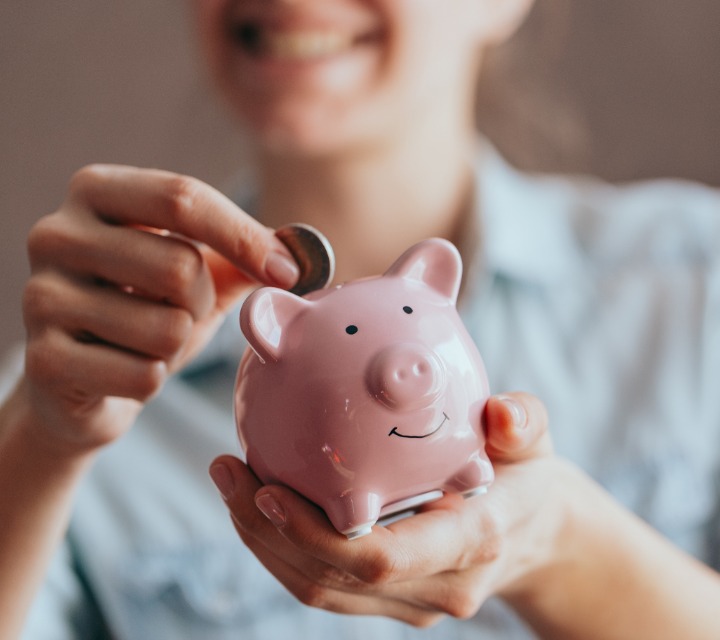 Woman Putting Coin In Pink Piggy Bank